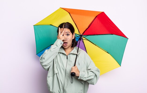 Bastante joven mirando conmocionado, asustado o aterrorizado, cubriéndose el rostro con la mano. concepto de lluvia y paraguas