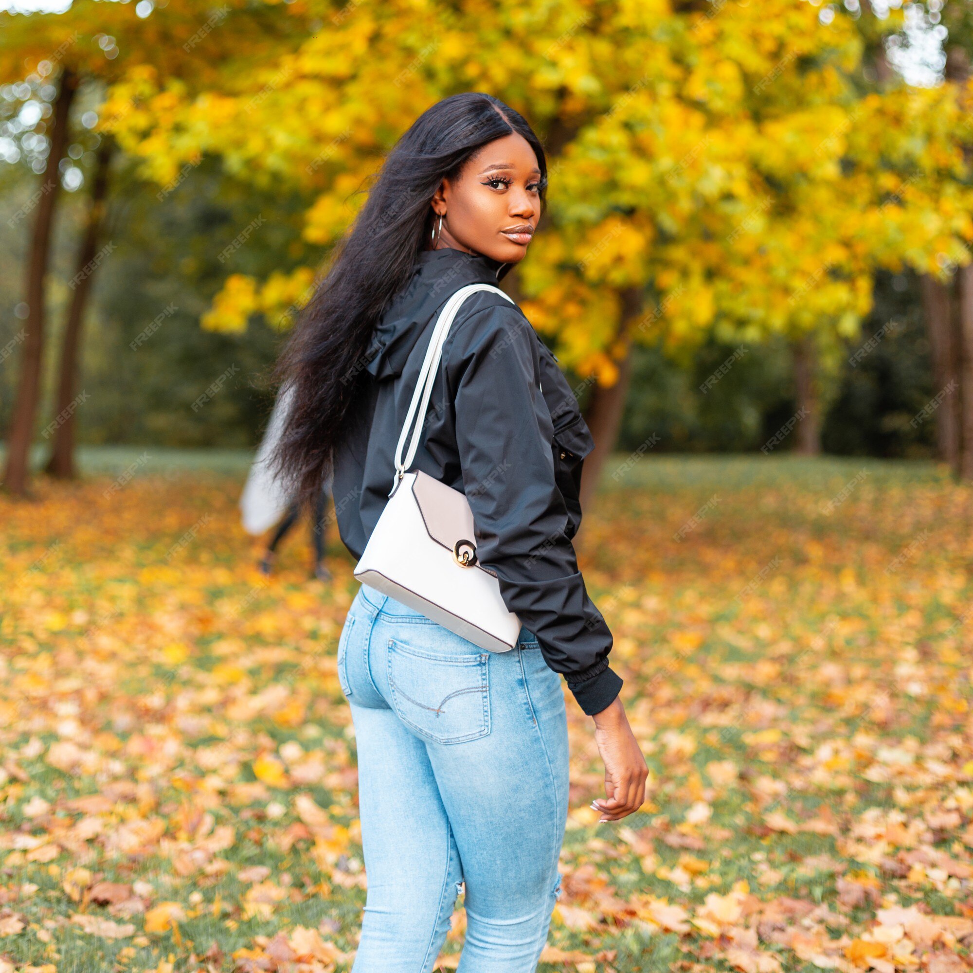 Bastante joven afroamericana sexy en ropa de moda con chaqueta casual, jeans y bolso elegante en el parque otoño con hojas otoño de color amarillo | Foto Premium