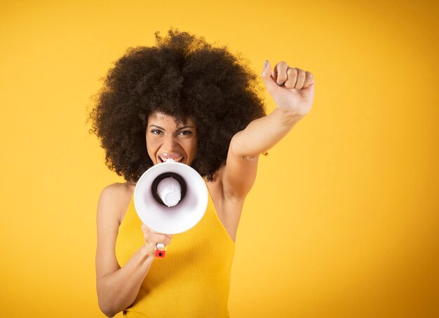 Bastante joven mujer afroamericana sonriendo con pelo rizado y gritando con megáfono