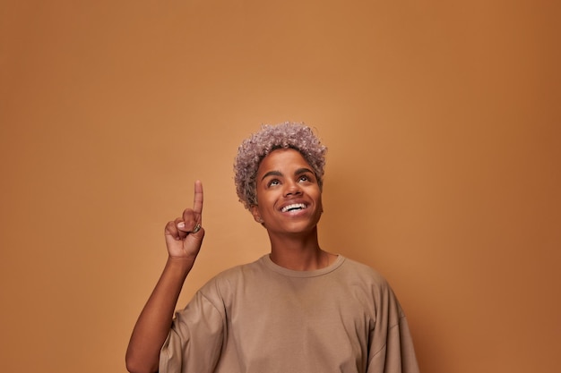 Bastante joven mujer afroamericana tiene cabello rizado claro sonrisa agradable hace gesto con índice fi...