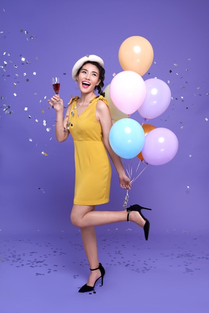 Bastante joven mujer asiática en la fiesta de celebración con globos de colores y copa de vino disfrutando con confeti cayendo por todas partes sobre ella. Feliz año nuevo o víspera de cumpleaños celebrando el concepto