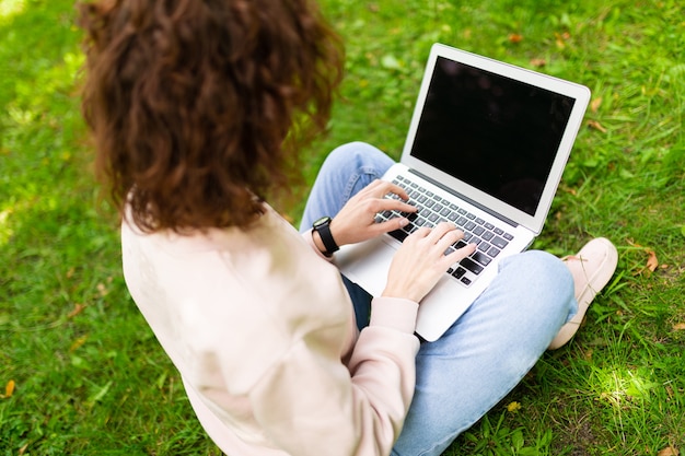 Bastante joven mujer caucásica se dedica a freelance en el parque con laptop