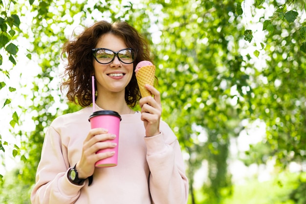 Bastante joven mujer caucásica ir a dar un paseo en el parque con café y helado