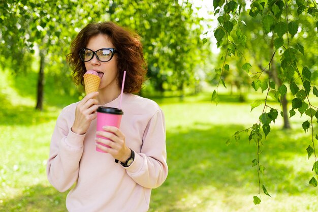 Bastante joven mujer caucásica ir a dar un paseo en el parque con café y helado