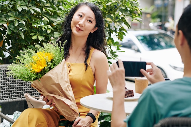 Bastante joven mujer china pidiendo novio que le haga una foto con un hermoso ramo de flores