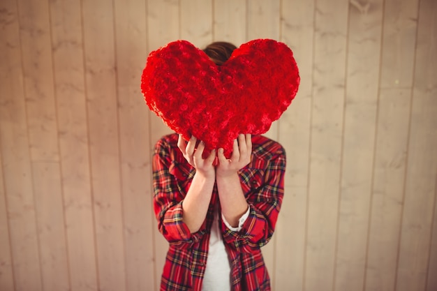 Foto bastante joven mujer escondiendo su rostro detrás de la almohada de corazón