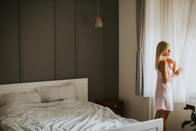 Bastante joven mujer junto a la ventana en la habitación