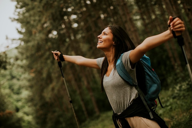 Bastante joven mujer mochilera disfrutando de un hermoso bosque verde a su alrededor