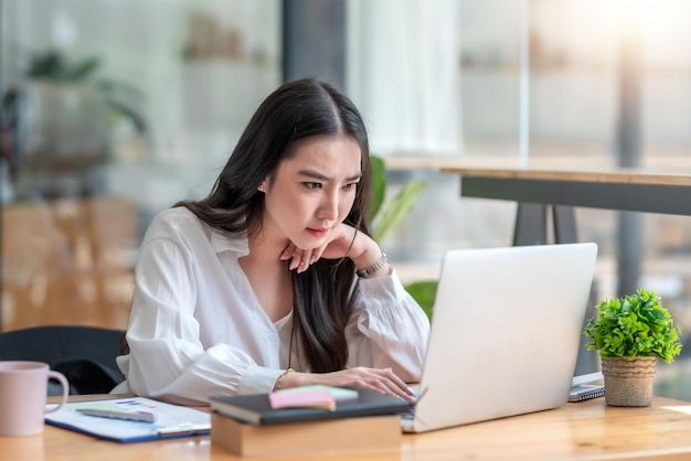 Bastante joven mujer de negocios asiática sentada en la oficina usando una computadora portátil