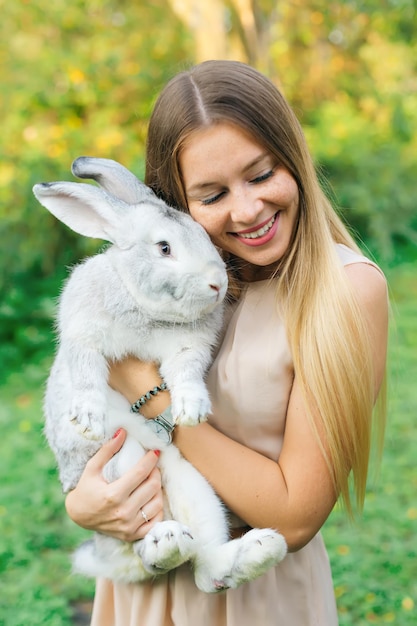 Bastante joven mujer de pelo largo abrazo lindo conejo en día de verano