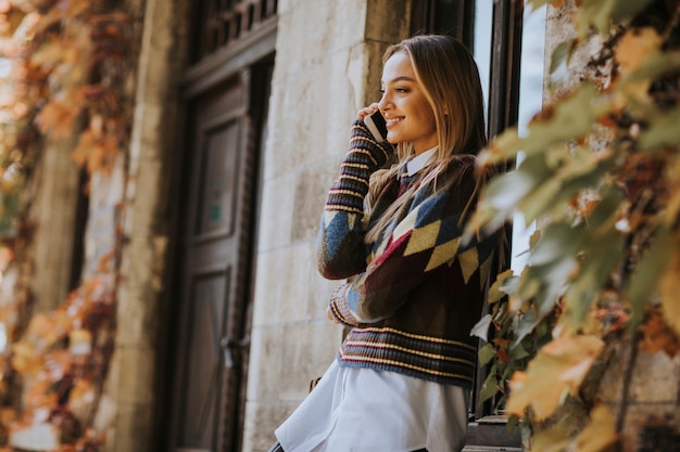 Foto bastante joven mujer de pie con el teléfono móvil en la calle en el día de otoño