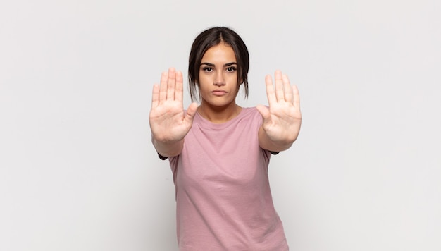 Bastante joven mujer que parece seria, infeliz, enojada y disgustada prohibiendo la entrada o diciendo que pare con ambas palmas abiertas