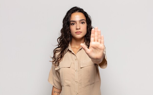 Bastante joven mujer que parece seria, severa, disgustada y enojada mostrando la palma abierta haciendo gesto de parada