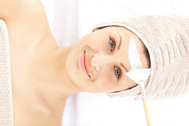 Foto bastante joven mujer recibiendo crema blanca en la cara