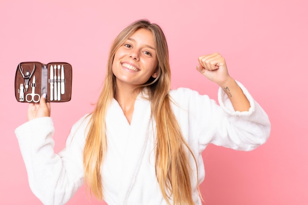 Bastante joven mujer rubia vestida con albornoz y sosteniendo una bolsa de maquillaje con herramientas de uñas