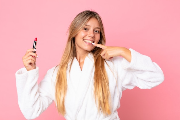 Bastante joven mujer rubia vestida con bata de baño y sosteniendo un lápiz labial