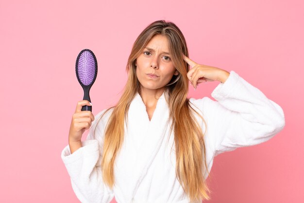 Bastante joven mujer rubia vistiendo albornoz y sosteniendo un cepillo de pelo