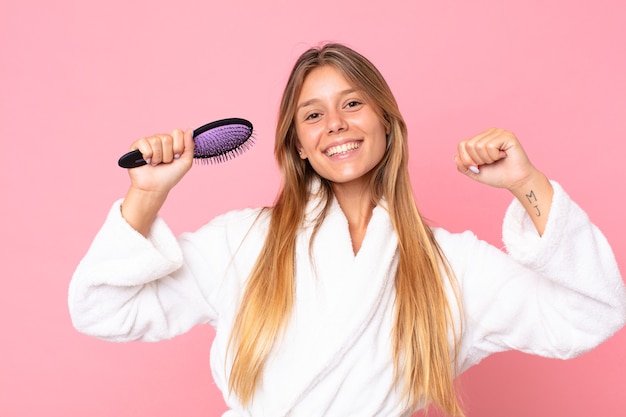 Bastante joven mujer rubia vistiendo albornoz y sosteniendo un cepillo de pelo