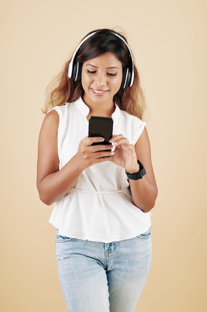 Bastante joven mujer sonriente usando audífonos cuando se usa la aplicación en el teléfono inteligente