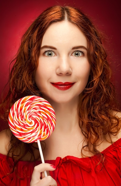 Foto bastante joven mujer sosteniendo lolly pop. sobre fondo rojo.