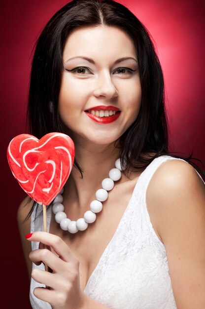 Bastante joven mujer sosteniendo lolly pop. Sobre fondo rojo.