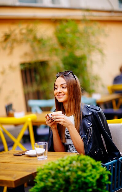 Bastante joven mujer tomando café en café en un día soleado