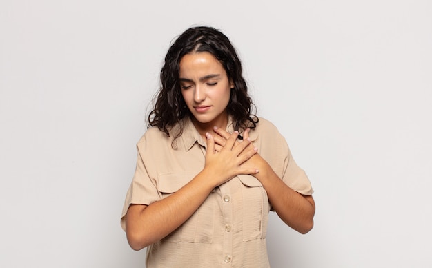 Bastante joven mujer triste, herida y desconsolada, sosteniendo ambas manos cerca del corazón