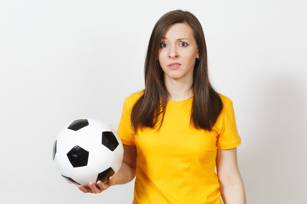 Bastante joven mujer triste molesta europea, aficionado al fútbol o jugador en uniforme amarillo tiene balón de fútbol, se preocupa por perder equipo aislado sobre fondo blanco. Deporte, jugar al fútbol, concepto de estilo de vida.