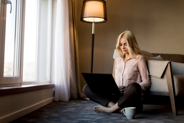 Bastante joven mujer usando la computadora portátil y sentado en el piso de la habitación