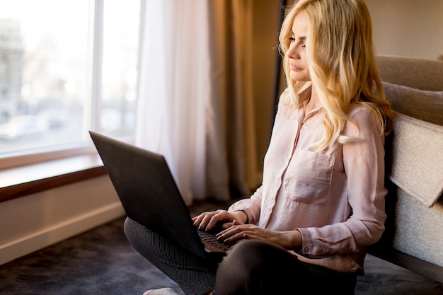 Bastante joven mujer usando la computadora portátil y sentado en el piso de la habitación