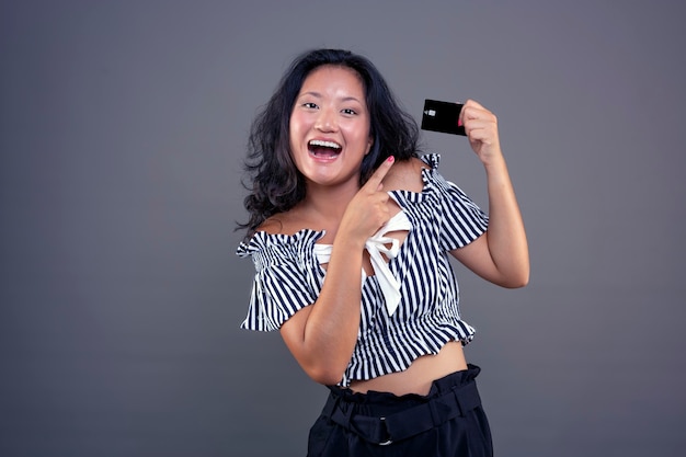 Bastante joven niña china feliz y sonriente mostrando tarjeta de crédito