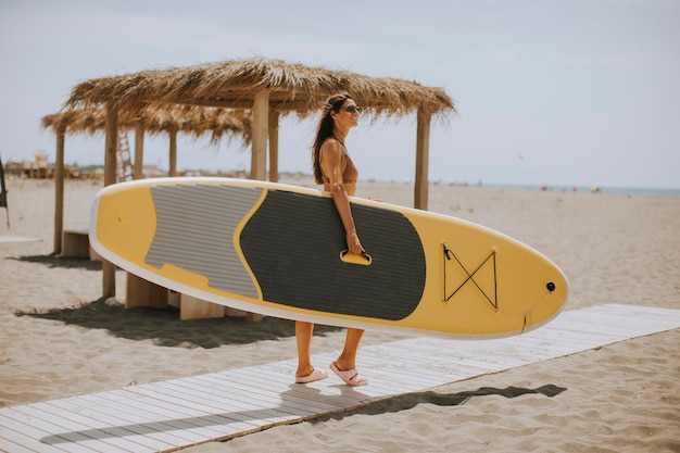 Bastante joven con paddle board en la playa en un día de verano