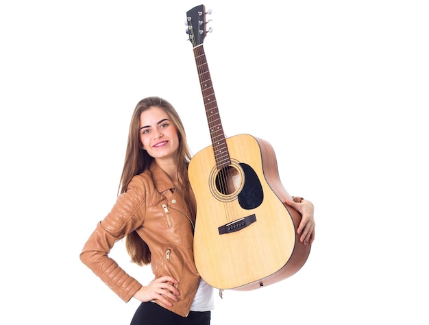 Bastante joven con el pelo largo en chaqueta marrón y pantalón negro sosteniendo una guitarra y sonriendo