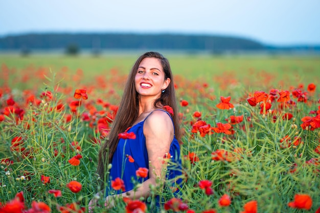 Bastante joven con el pelo largo jugando con pétalos en el campo de amapolas en la luz del sol de la tarde