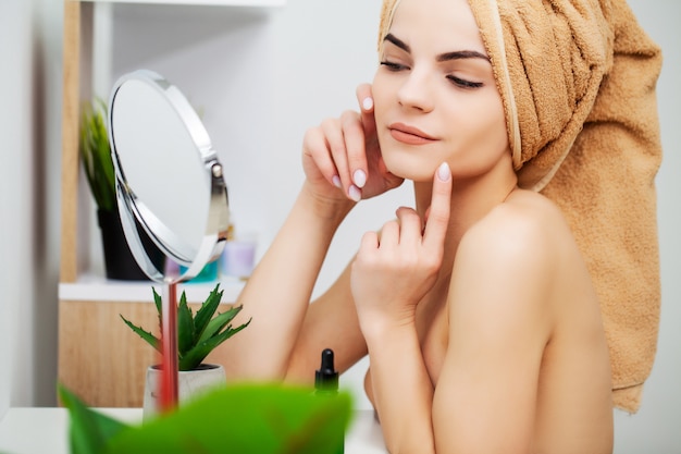 Bastante joven pone maquillaje en la cara en el baño.