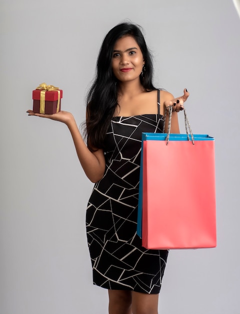 Bastante joven posando con bolsa de compras y caja de regalo sobre un fondo gris