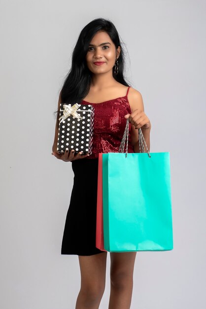 Bastante joven posando con bolsa de compras y caja de regalo sobre un fondo gris