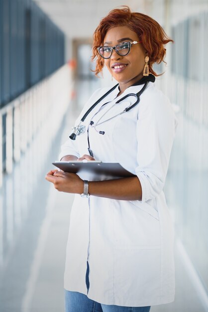 Bastante joven profesional médico afroamericano de pie y mirando a cámara en un hospital.