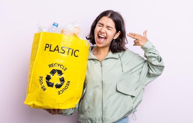 Bastante joven que parece infeliz y estresada, gesto de suicidio haciendo señas de armas. concepto de reciclaje de plástico