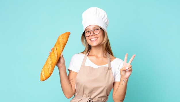 Bastante joven rubia chef mujer sosteniendo una baguette de pan