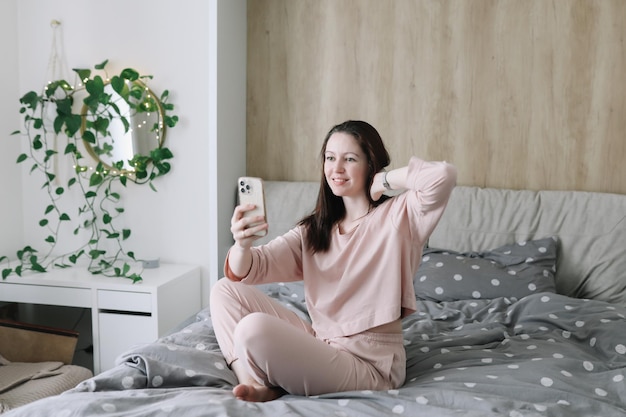 Bastante joven sentada en la cama y hace selfie