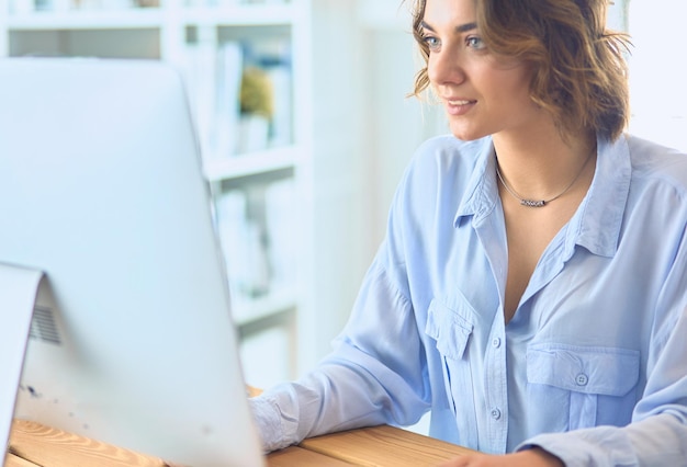 Foto bastante joven sentada en el escritorio y escribiendo en la computadora portátil