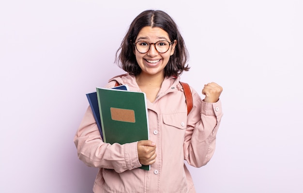 Bastante joven sintiéndose conmocionada, riendo y celebrando el éxito. estudiante con concepto de libros