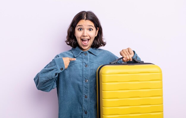 Bastante joven sintiéndose feliz y apuntando a sí mismo con un emocionado. concepto de estuche de viaje