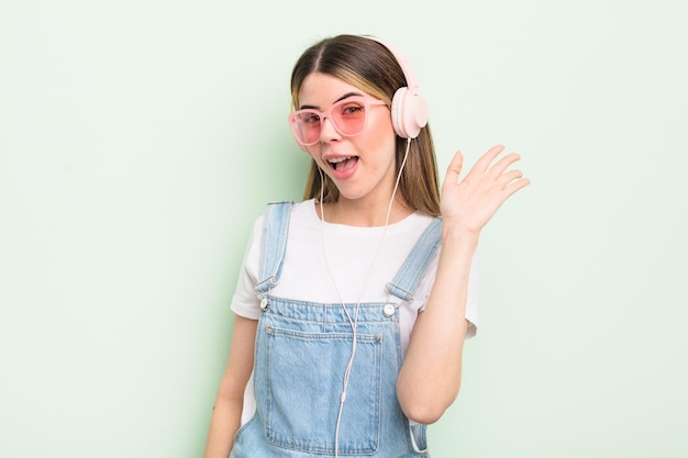 Bastante joven sonriendo alegremente saludando con la mano dándole la bienvenida y saludándole escuchando el concepto de música