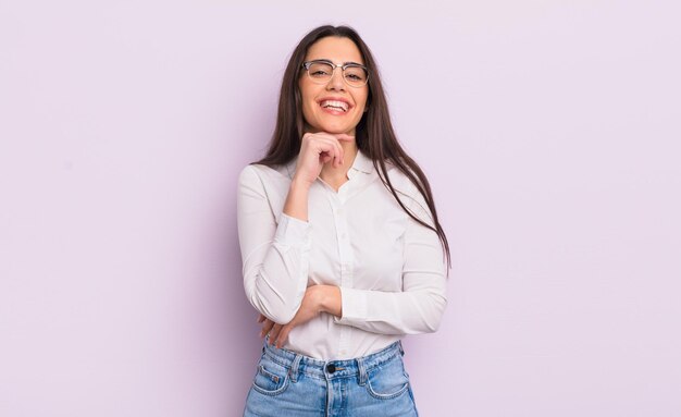 Bastante joven sonriendo, disfrutando de la vida, sintiéndose feliz, amigable, satisfecha y despreocupada con la mano en la barbilla