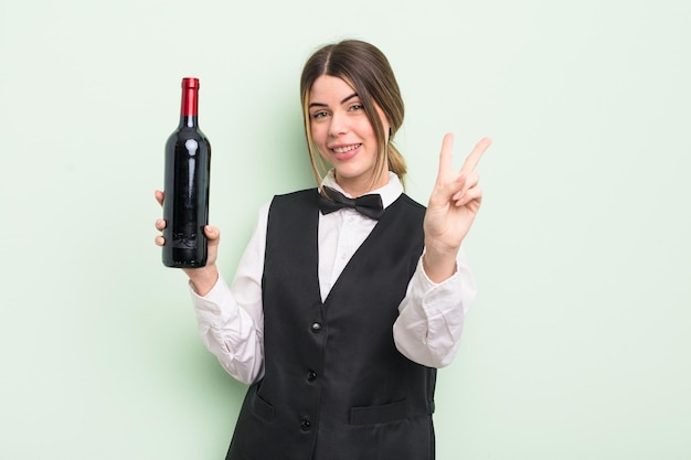 bastante joven sonriendo y luciendo amigable, mostrando el número dos. concepto de camarero y botella de vino