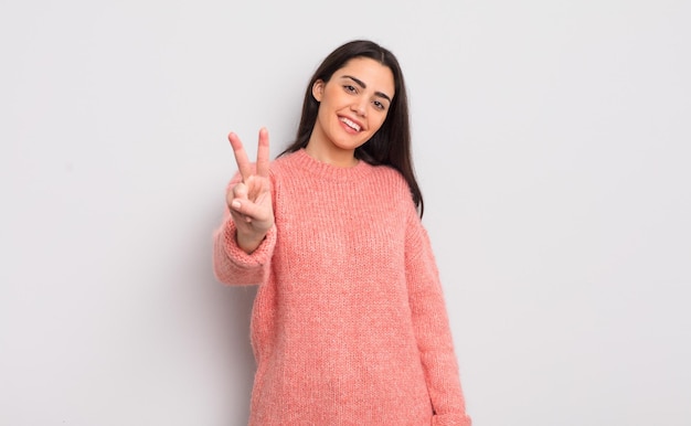 Bastante joven sonriendo y luciendo amigable mostrando el número dos o segundo con la mano hacia adelante contando hacia atrás