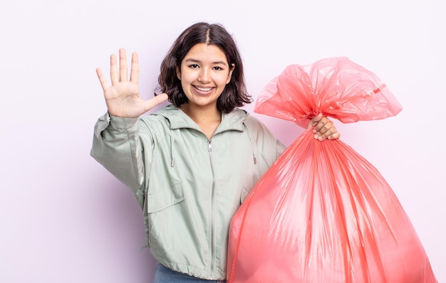 Bastante joven sonriendo y mirando amigable, mostrando el número cinco. concepto de bolsa de basura