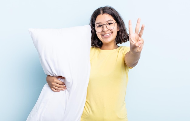 Bastante joven sonriendo y mirando amigable, mostrando el número tres. concepto de cama